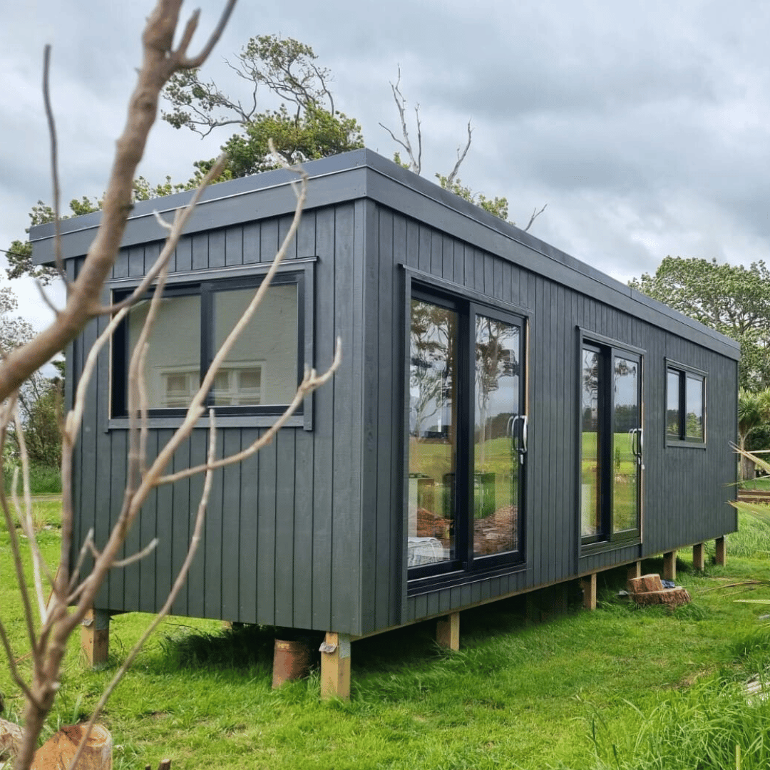 black cabin sitting on piles in a grassy area